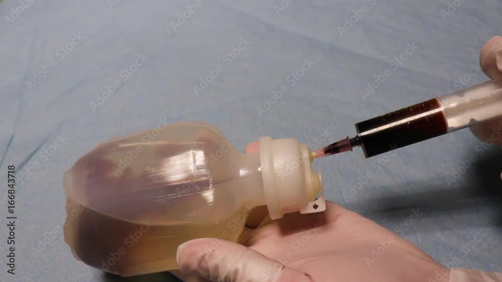 Hands in gloves add a dark liquid to the vial of the medicine.