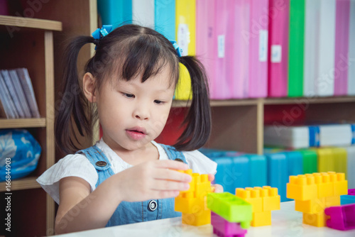Little asian preschool age girl playing plastic blocks at nursery