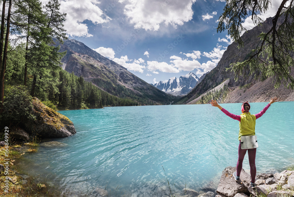 Woman traveler with open arms admiring the view of the famous beautiful turquoise lake Shavla in the mountains of Altai, Russia