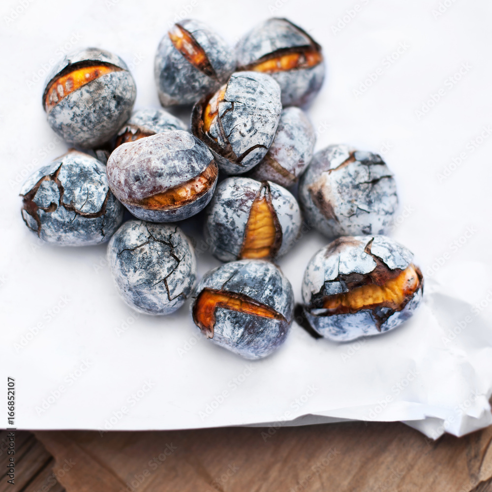 Roasted chestnuts served on white and brown craft paper with copy space. Delicious grilled chestnuts on old wooden table close up. Roasted chestnuts served on white and brown craft paper with copy space. Delicious grilled chestnuts on old wooden table close up.