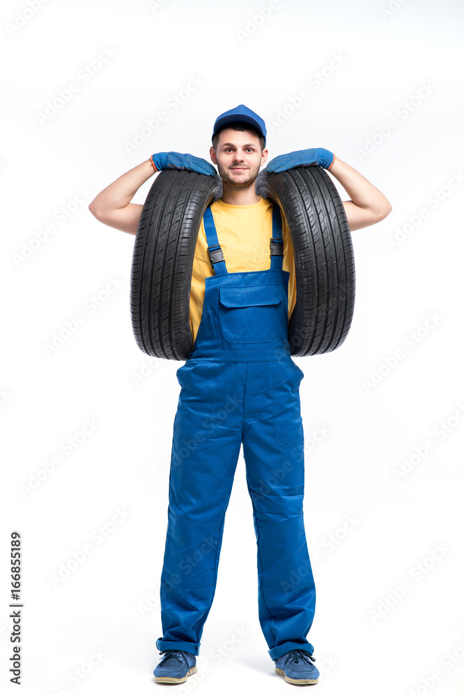 Tire service worker in blue uniform holds car tyre Tire service worker in blue uniform holds car tyre