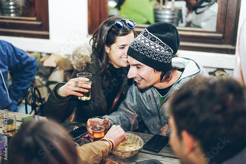 Happy rich friends toasting beers at chalet pub restaurant in mountains on evening time - Young people having fun in winter vacation - Friendship concept - Soft focus on woman face - Warm filter photo