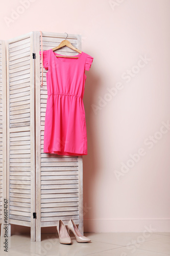 Pink dress hanging on folding screen on a beige background