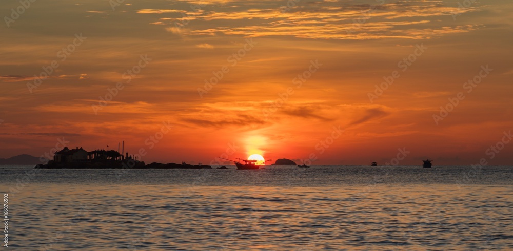 Obraz premium A fiery orange sunrise sky looking out over the south China sea in Nha Trang Bay Vietnam. With fishing boats in silhouette.