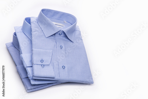 Three blue men's shirts folded in a pack on a white background. © nadyanadal