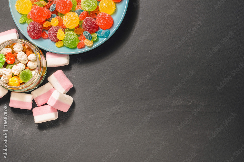 Bright colored candy, candy, marshmallow, sweets on a dark background on blue plate, top view Bright colored candy, candy, marshmallow, sweets on a dark background on blue plate, top view