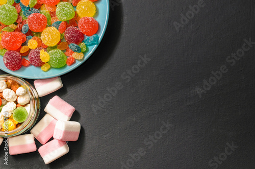 Bright colored candy, candy, marshmallow, sweets on a dark background on blue plate, top view