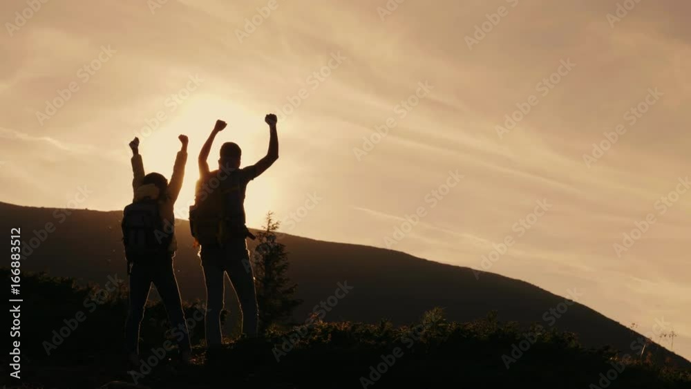 A pair of mountaineers with backpacks behind their back hitting each other in the rays of the setting sun. Success on top and leadership A pair of mountaineers with backpacks behind their back hitting each other in the rays of the setting sun. Success on top and leadership