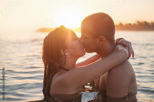 Romantic young couple hugging, kissing on the beach at sunset, in water