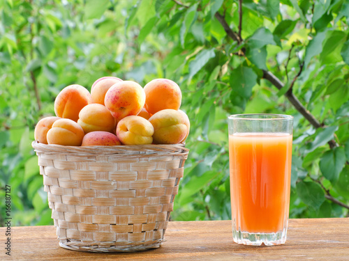 Apricots in a wicker basket and a glass of juice on a green background, sunlight