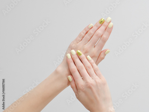 Beautiful female hands with a manicure on a light background. Yellow with gold nails