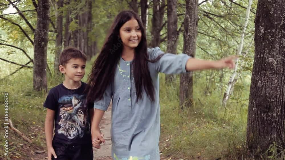 Cute happy little brother and sister are walking holding hands smiling in sunny summer weather