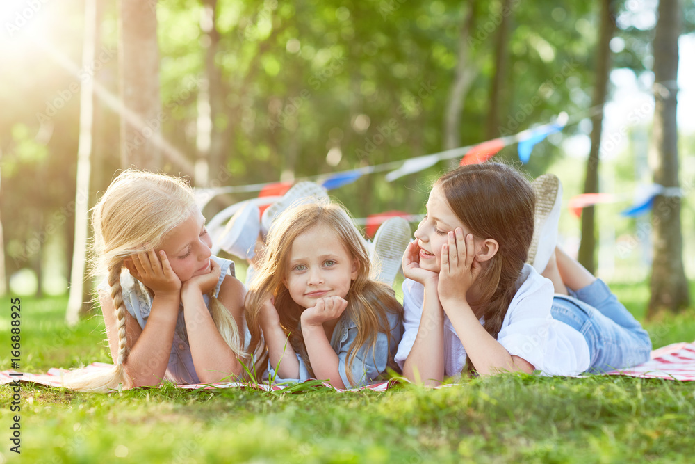 Naklejka premium Three cute girls relaxing on green lawn in summer park