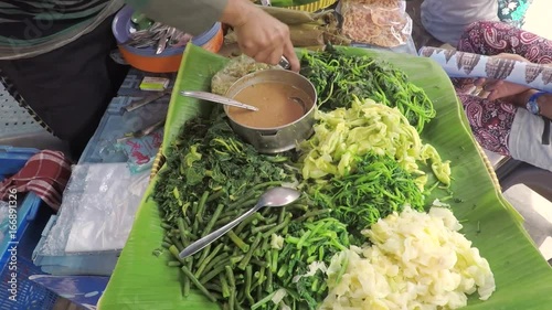 Yogyakarta, Indonesia. August 02, 2017: Video footage of seller makes Pecel Indonesian traditional food from boiled vegetables and peanut sauces photo
