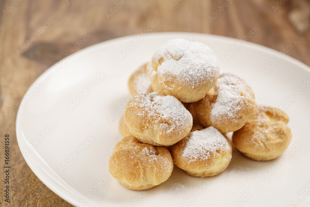 closeup shot of profiteroles covered with sugar powder on white plate on wooden table