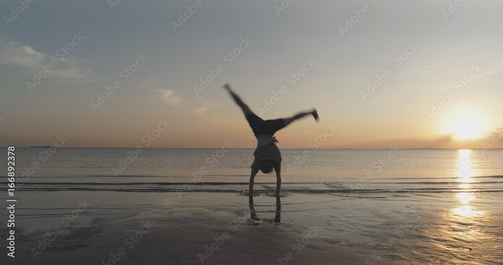 teen girl doing cartwheel on a beach in sunset time motion blur