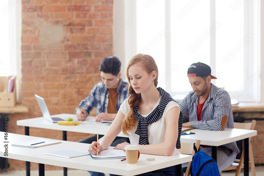 Young managers writing examination essay by desks Young managers writing examination essay by desks