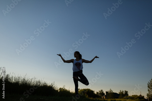 Woman doing yoga outdoor. Young woman exercising meditation for fitness lifestyle at the nature background with blue sky. Concept Yoga freedom silhouette on sunset  full length shot with copy space