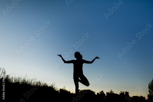 Woman doing yoga outdoor. Young woman exercising meditation for fitness lifestyle at the nature background with blue sky. Concept Yoga freedom silhouette on sunset, full length shot with copy space