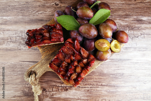 rustic plum cake on wooden background with plums around