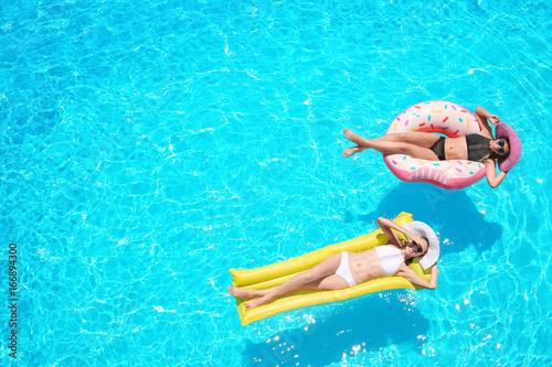 Beautiful young girls with inflatable donut and mattress in blue swimming pool
