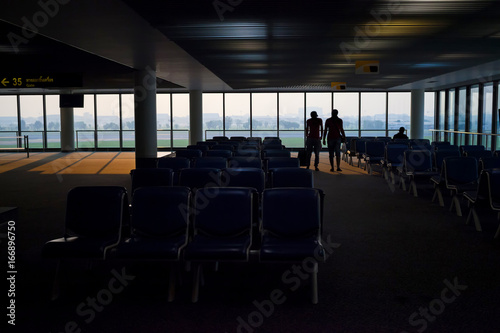 The silhouette view of a travelers are waiting in terminal with panoramic windows.