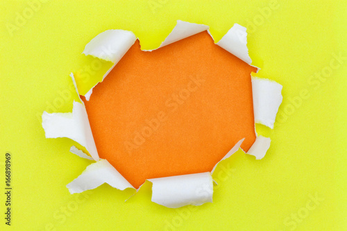 Torn hole and ripped of yellow paper with space for text with orange background.