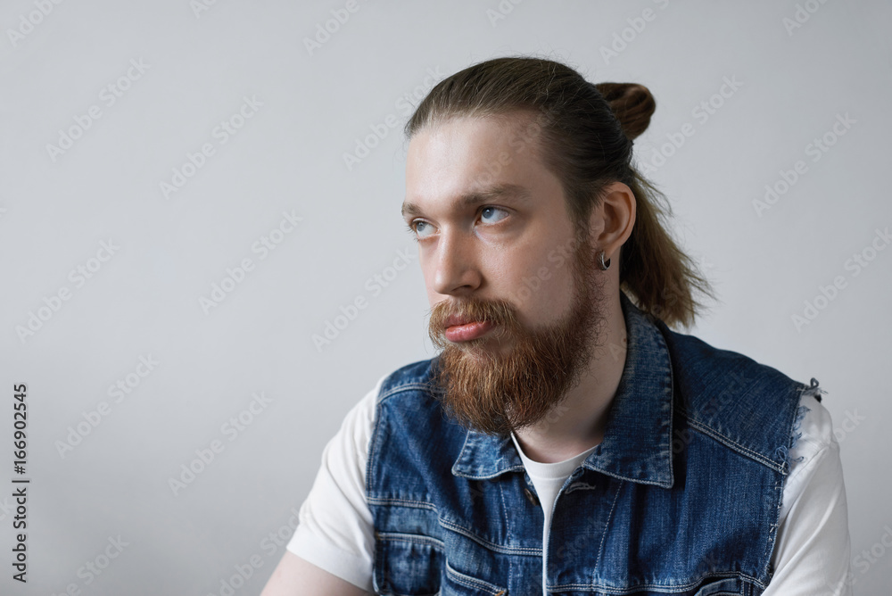Headshot of fed-up young European hipster man with facial hair and bun rolling his eyes while feeling annoyed or irritated with something, having displeased and bored look. Human emotions and feelings Headshot of fed-up young European hipster man with facial hair and bun rolling his eyes while feeling annoyed or irritated with something, having displeased and bored look. Human emotions and feelings