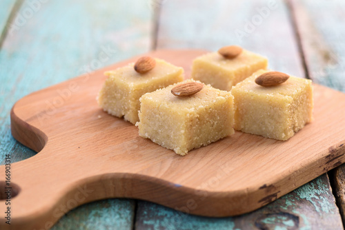 Schilderij op canvas Homemade tasty semolina halva with whole almonds cut in squares on wooden board