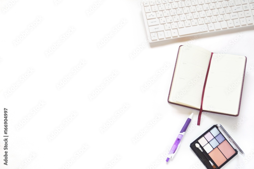 Flat lay work place/ White computer keyboard, open notepad, purple pen and eyeshadow Flat lay work place/ White computer keyboard, open notepad, purple pen and eyeshadow
