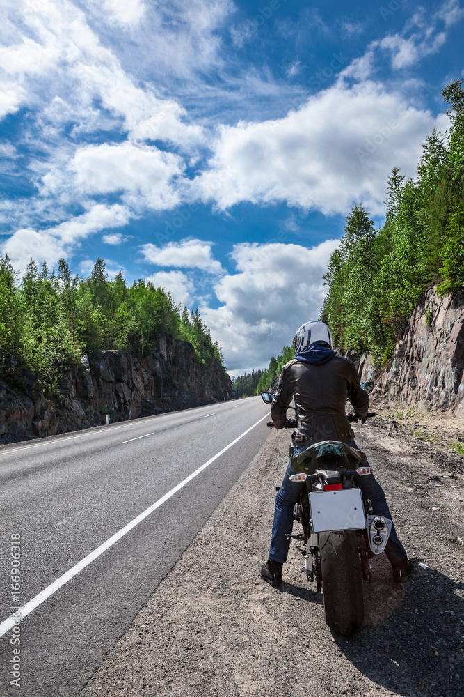 Motorcycle driver is ready to start driving on the asphalt road, sitting on motorbike, rear view Motorcycle driver is ready to start driving on the asphalt road, sitting on motorbike, rear view