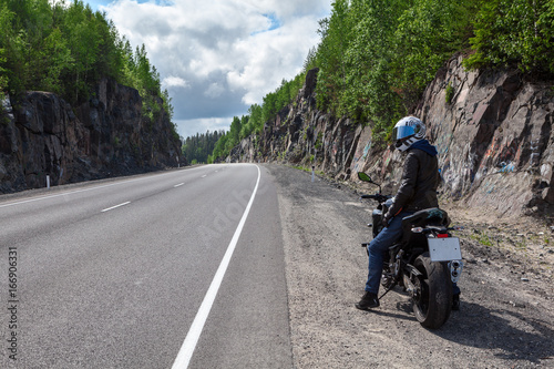 Man with modern naked motorbike turning back while standing on roadside of the mountain asphalt road  rear view  copyspace