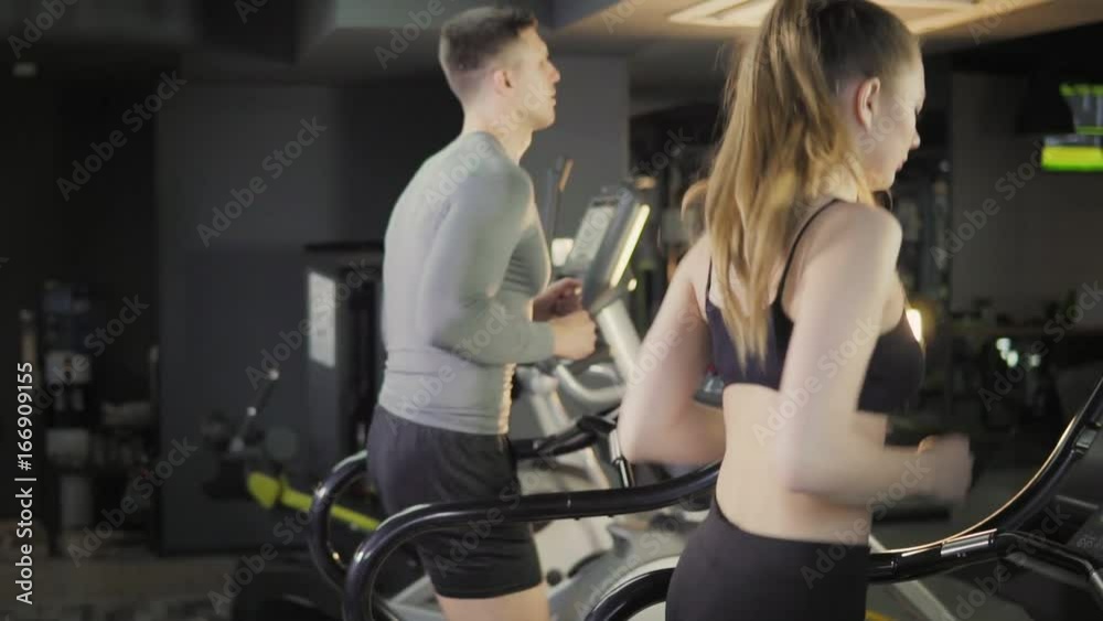 Young men and women of athletic build in the gym on a treadmill Young men and women of athletic build in the gym on a treadmill