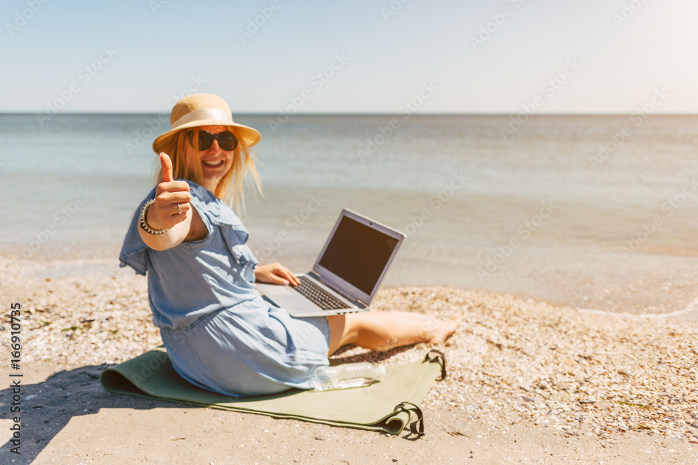 Young beautiful woman sitting with laptop on the beach near the sea