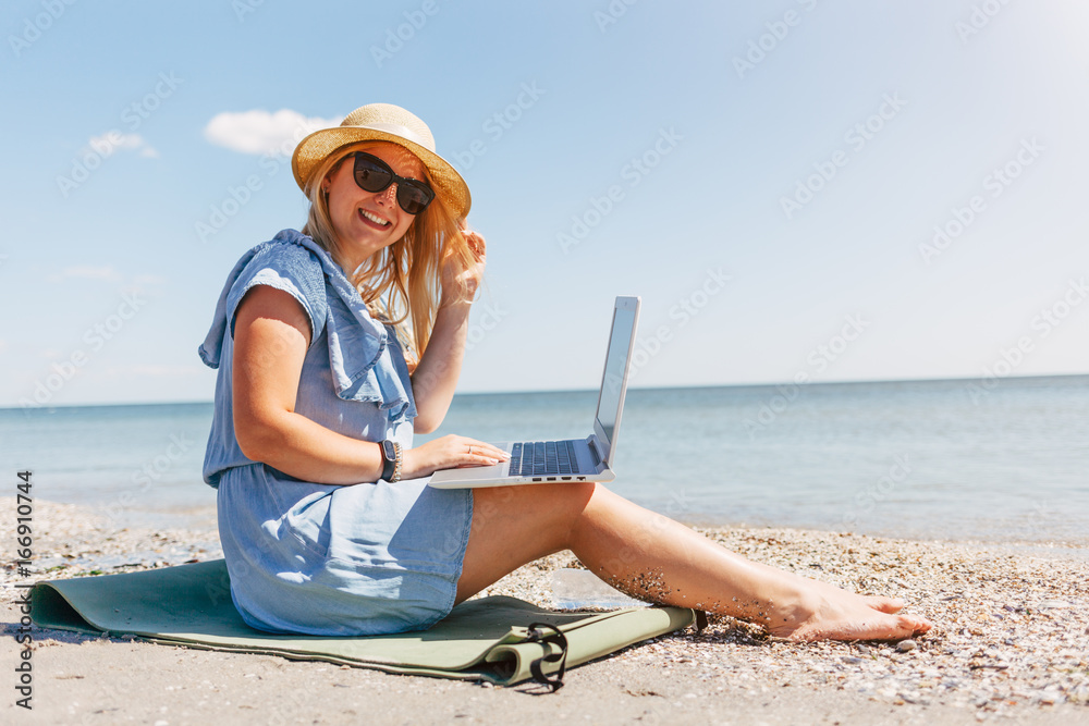 Young beautiful woman sitting with laptop on the beach near the sea