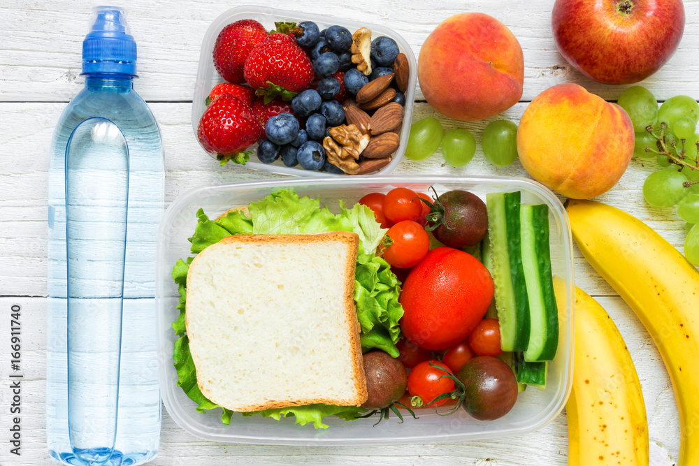 School lunch boxes with sandwich, fresh fruits and vegetables, berries and nuts and bottle of water School lunch boxes with sandwich, fresh fruits and vegetables, berries and nuts and bottle of water