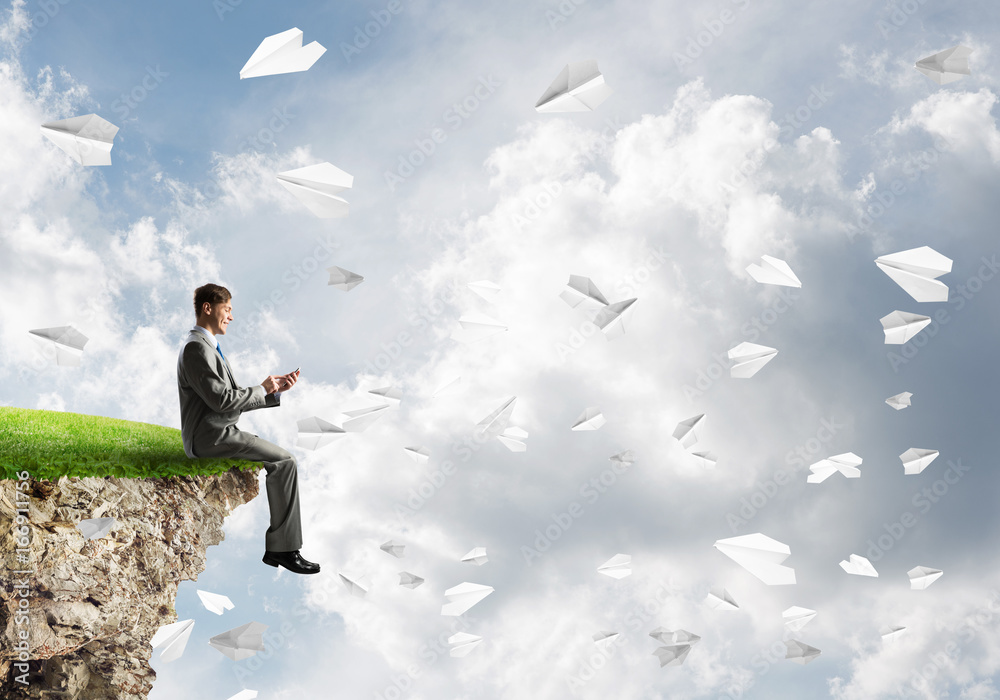 Elegant businessman on rock edge making calls and paper planes flying around Elegant businessman on rock edge making calls and paper planes flying around