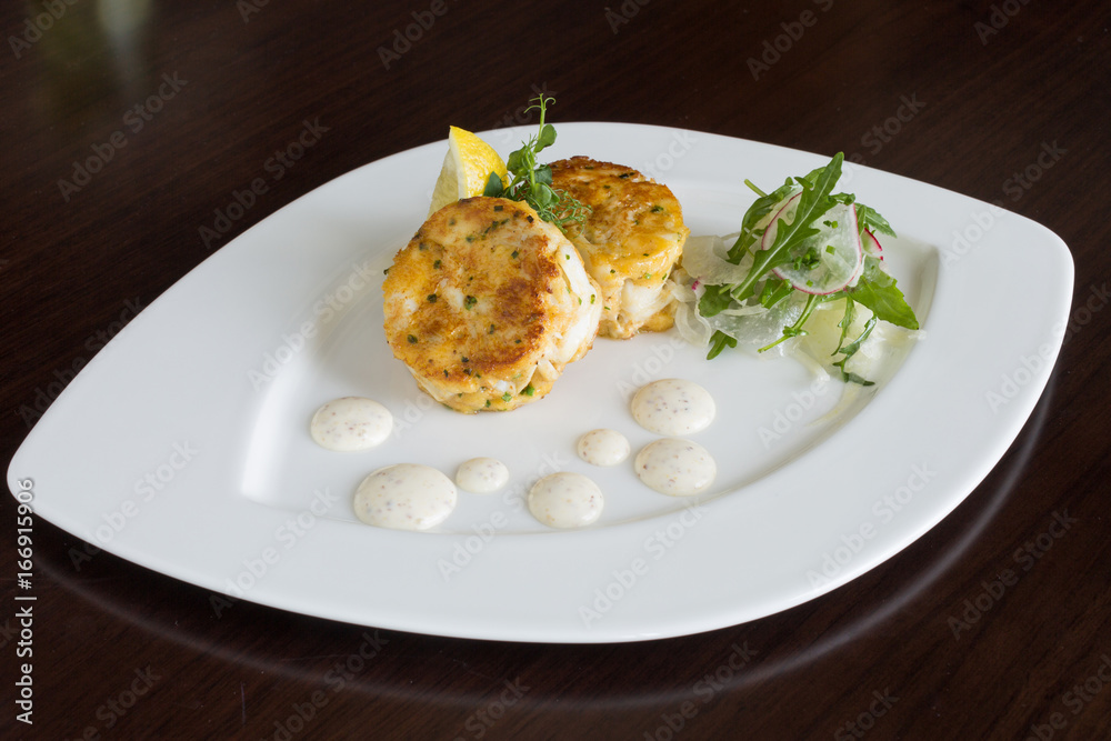 Beautiful fresh golden fish cakes, served with a wedge of lime, dill sauce and rocket on a white plate