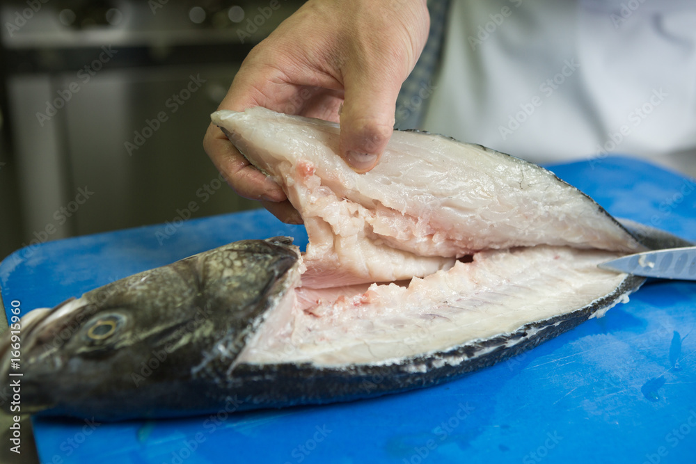 Filleting and removing the bone from a fresh fish on a blue cutting board using a sharp knife. Filleting and removing the bone from a fresh fish on a blue cutting board using a sharp knife.