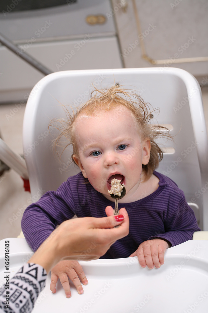 Fototapeta premium Mother feeds baby boy with a spoon porridge