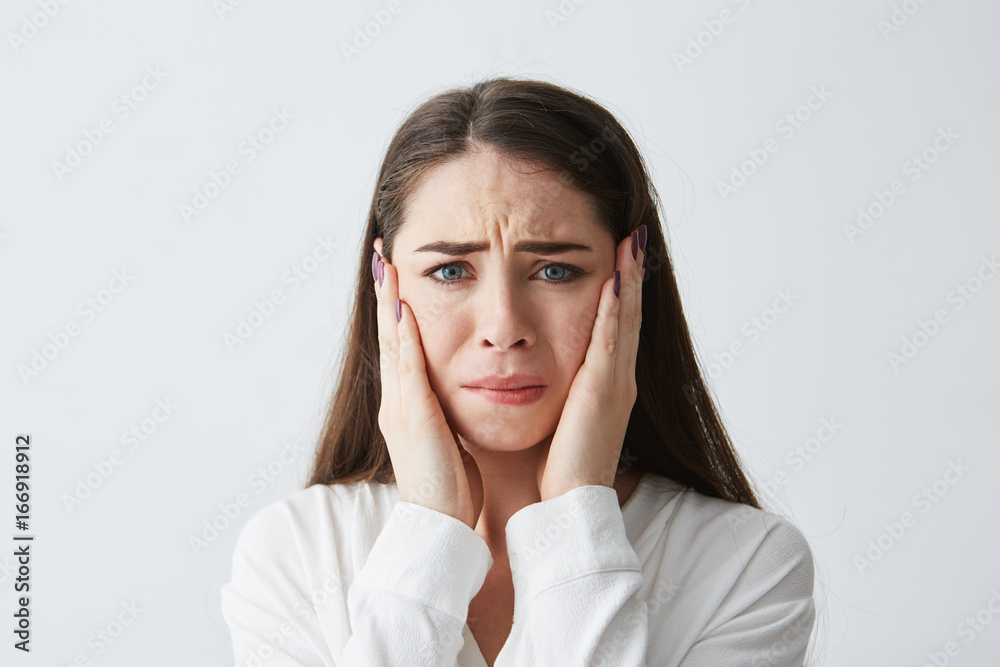 Sad upset young girl looking at camera with hands on face over white background. Sad upset young girl looking at camera with hands on face over white background.