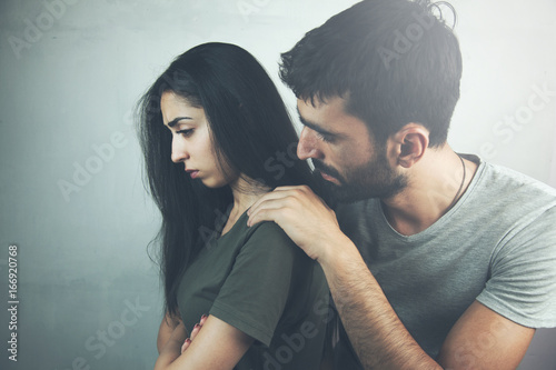 Depressed young woman looking away while man sitting behind her on the couch and consoling her