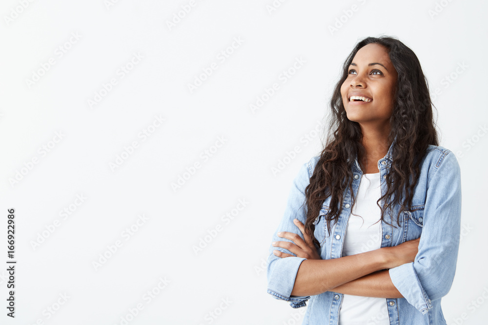 Indoor shot of beautiful happy Afro-American female employee standing isolated on white studio smiling cheerfully, keeping her arms folded, relaxing indoors after work. Indoor shot of beautiful happy Afro-American female employee standing isolated on white studio smiling cheerfully, keeping her arms folded, relaxing indoors after work.
