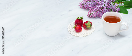 Lilac blossom branches, cup of tea and strawberries on Carrara marble countertop
