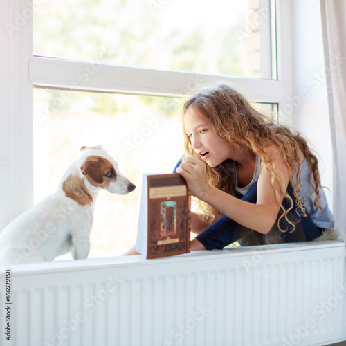 Girl reading book at home with dog