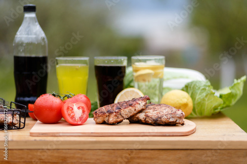 Chicken breast grilled on a wooden Board. Food photography chicken chili steak on the background with vegetables and black soda and lemonade. Food and summer drinks for a picnic in the fresh air.