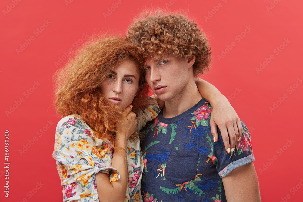 Young fashion models posing at studio wall, standing close to each other and embracing, looking at camera with serious confident expression on their faces. People, style and fashion concept Young fashion models posing at studio wall, standing close to each other and embracing, looking at camera with serious confident expression on their faces. People, style and fashion concept