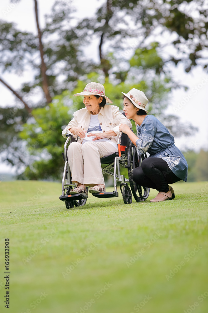 Elderly woman relax on wheelchair in backyard with daughter Elderly woman relax on wheelchair in backyard with daughter