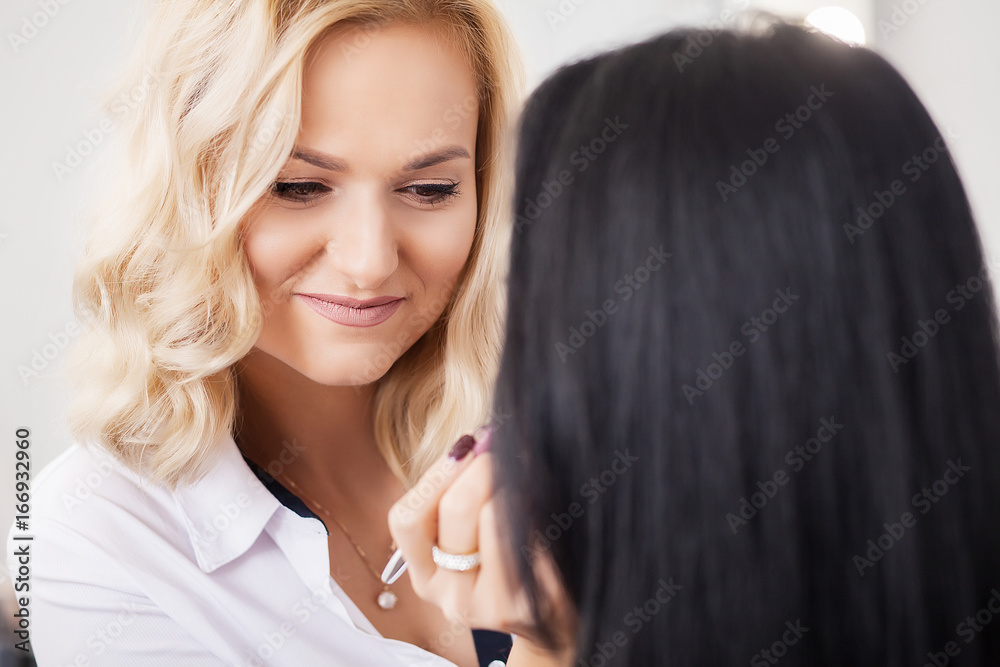 Fototapeta premium Backstage scene: Professional Make-up artist doing makeup for young businesswoman at beauty salon. Close up