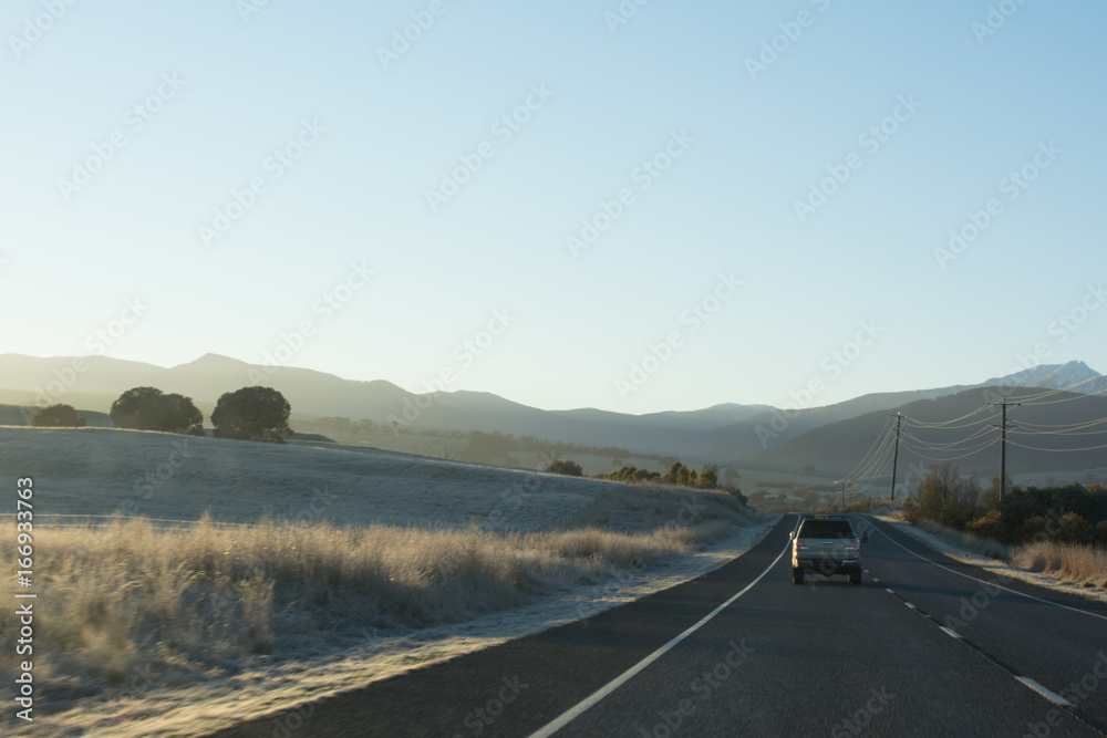 Country highway with cars leading towards mountains at sunrise